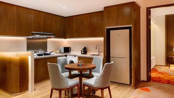 Een moderne keuken met houten kastjes, een inbouwoven en een eethoek met twee stoelen.