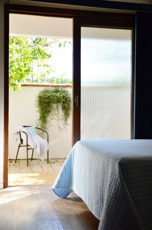 Un dormitorio con una cama, vistas a un balcón con una silla y una planta, y una puerta que da al exterior.