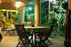 An outdoor dining area with a round table and chairs, surrounded by lush greenery and a statue.