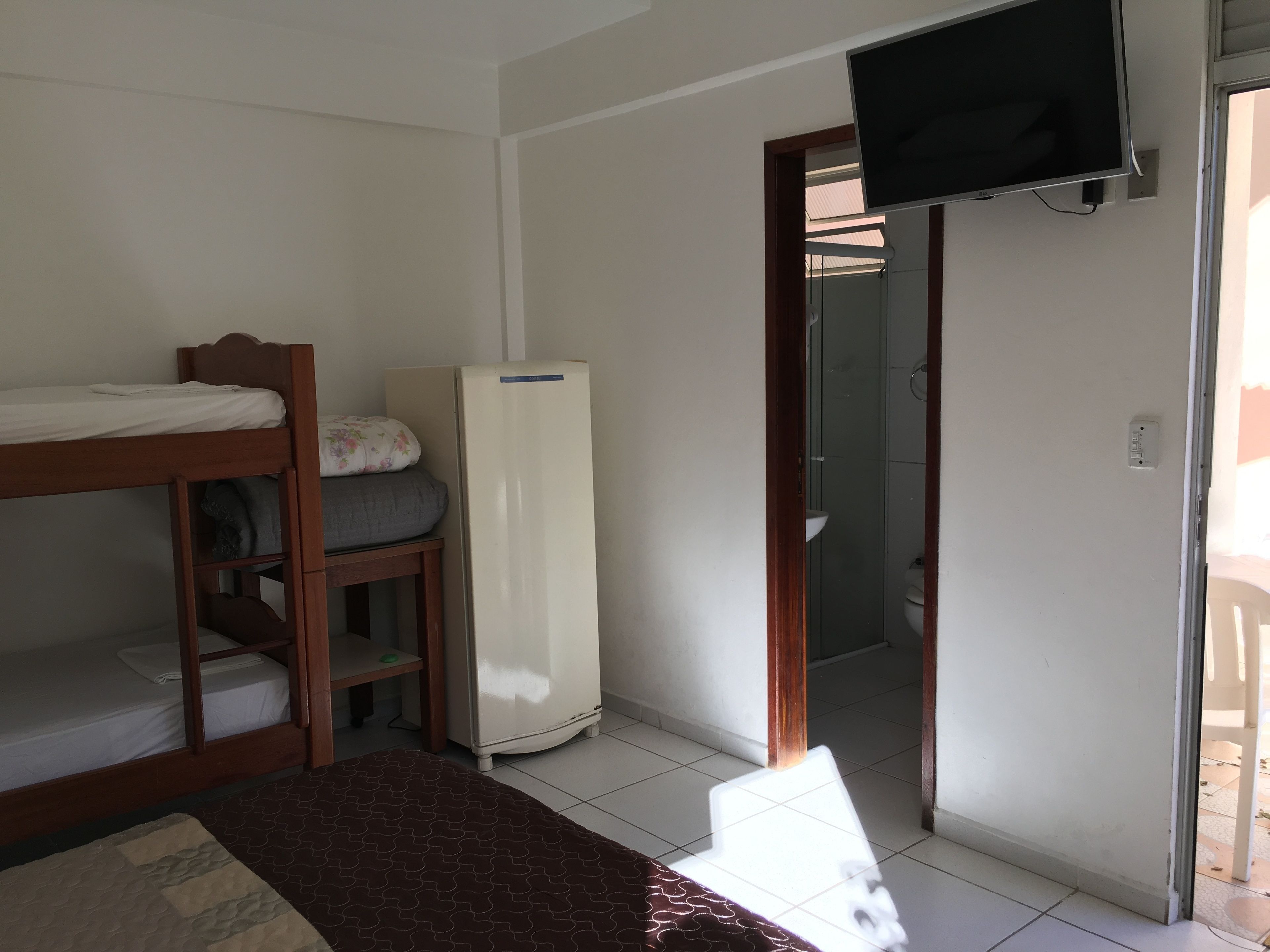 Une chambre équipée d’un lit superposé, d’un réfrigérateur, d’un téléviseur fixé au mur et d’une porte donnant accès à une salle de bain.
