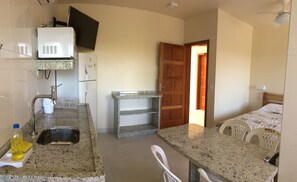 Una cocina compacta con refrigerador, pileta y una pequeña mesada. Una puerta de madera da a otra habitación.