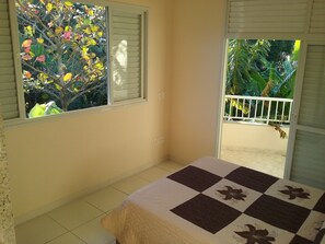 Una habitación con cama, ventana con persianas y vistas a un balcón con plantas.