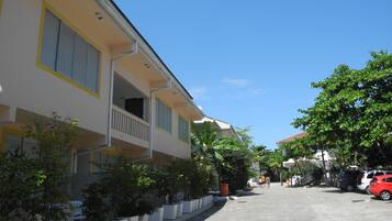 A two-story building with a balcony, potted plants, and a paved street.