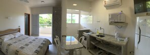 Un dormitorio con cama y balcón, una kitchenette con estufa, pileta y microondas, además de un refrigerador.
