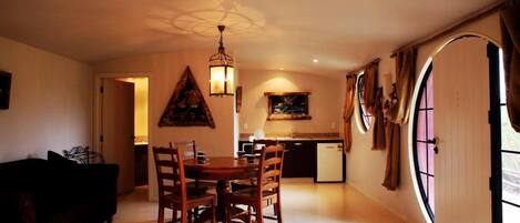 A cozy dining area with a wooden table and chairs, a hanging light fixture, and a kitchen in the background.