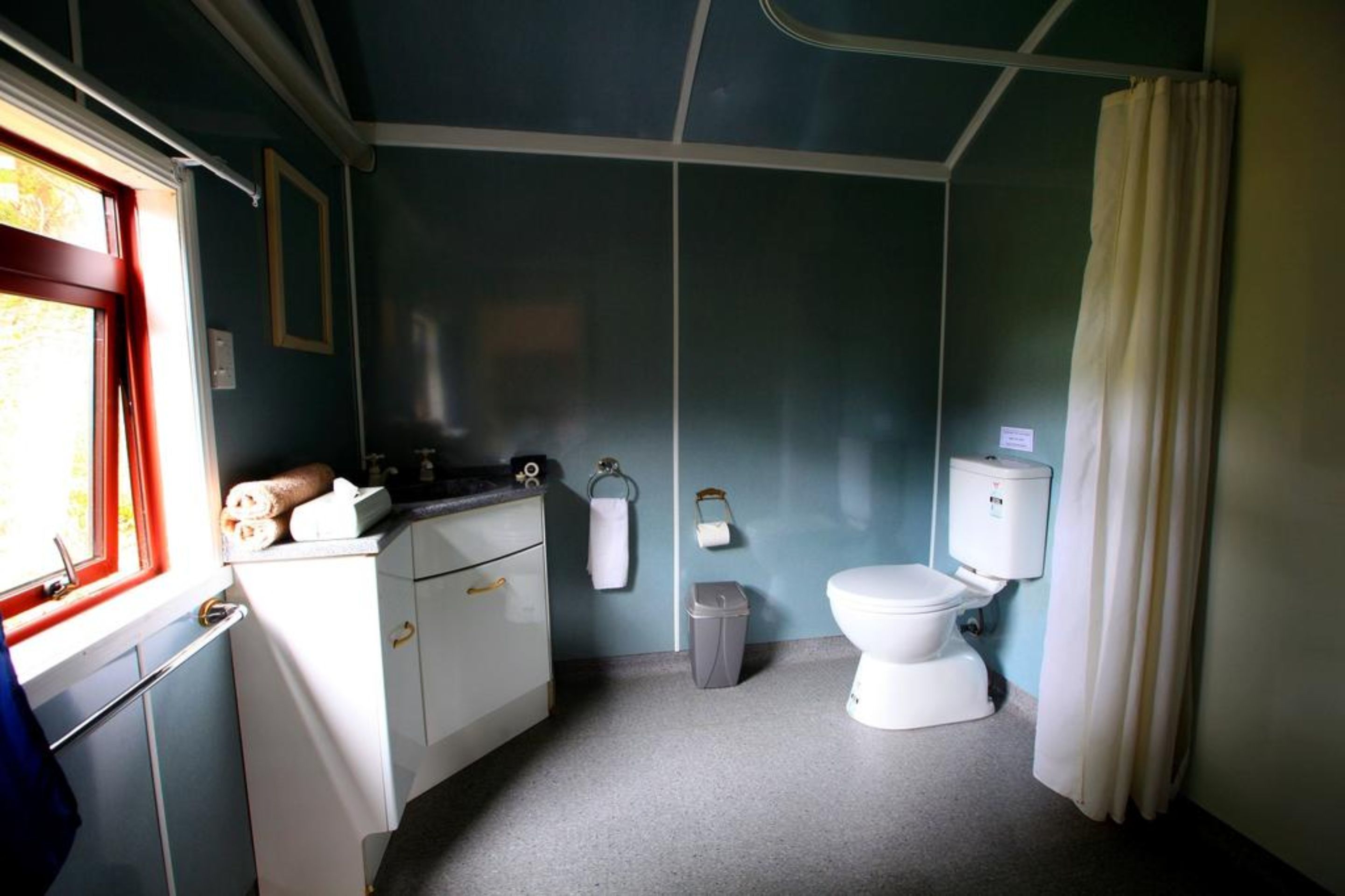 A compact bathroom with a toilet, sink, and a window with a red frame.