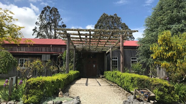 A rustic building with a red roof, a wooden pergola, and a gravel pathway leading to the entrance. - Woodlyn Park (Waitomo Caves)