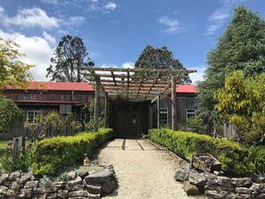 A rustic building with a red roof, a wooden pergola, and a gravel pathway leading to the entrance. - Woodlyn Park (Waitomo Caves)