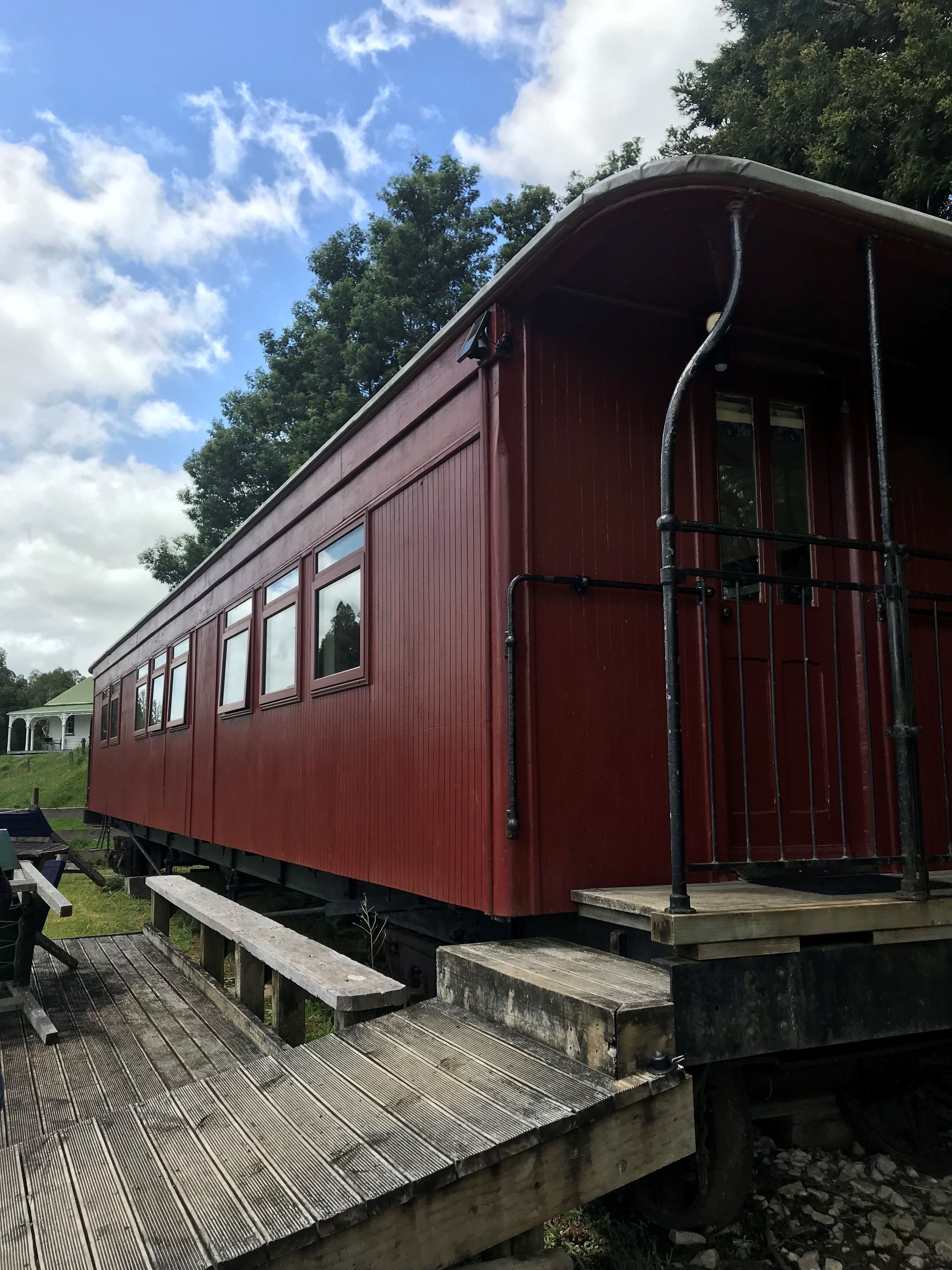 Un vagó vermell de tren amb una plataforma coberta, finestres i una barana metàl·lica.