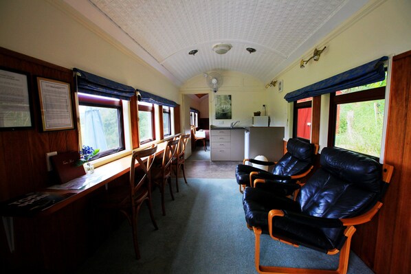 Un vagón de tren con paneles de madera, un comedor con mesas y sillas, una zona de cocina y un área de descanso con sillones de cuero.