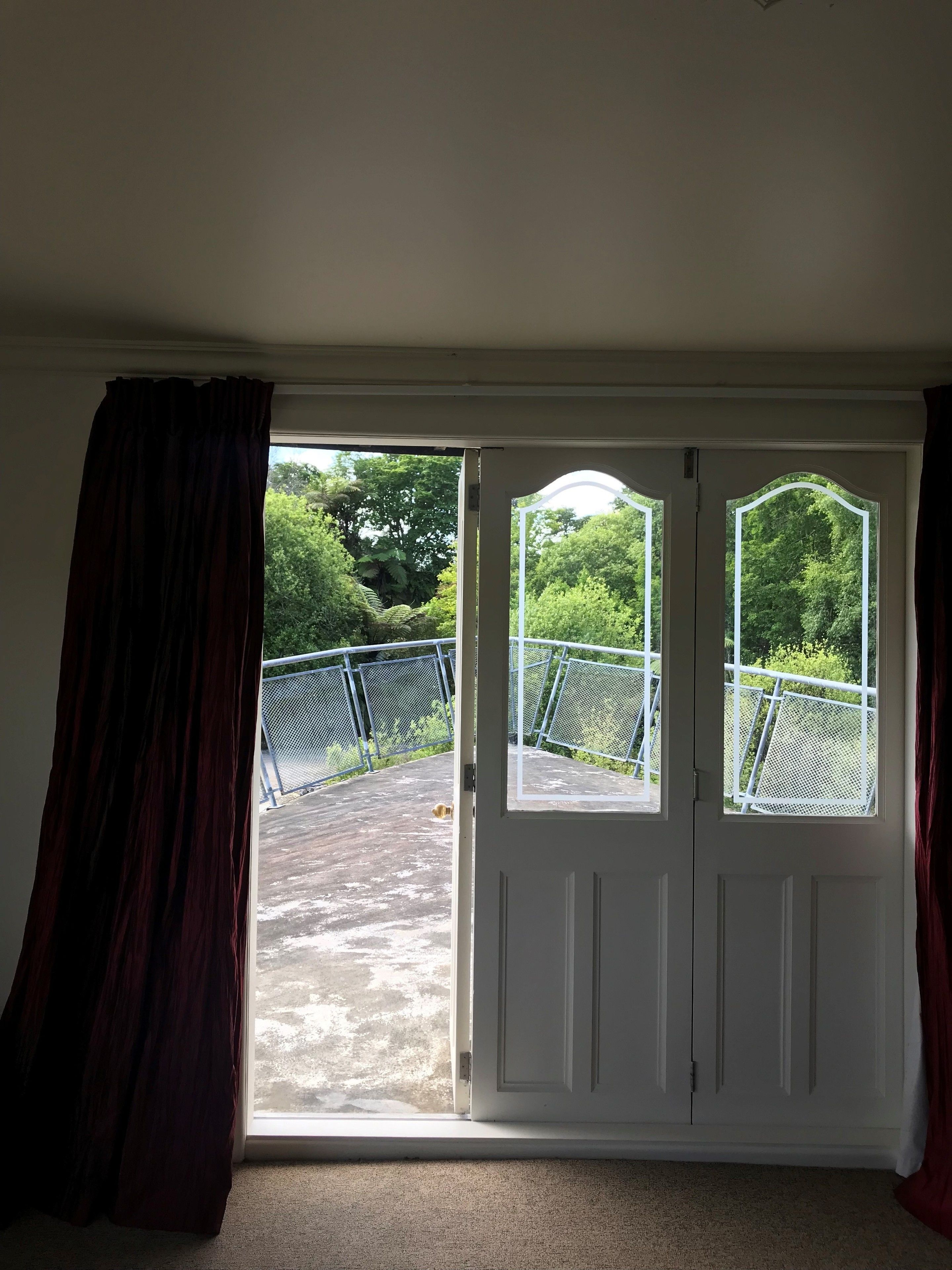 A room with a large sliding glass door leading to an outdoor area with a metal fence and greenery.