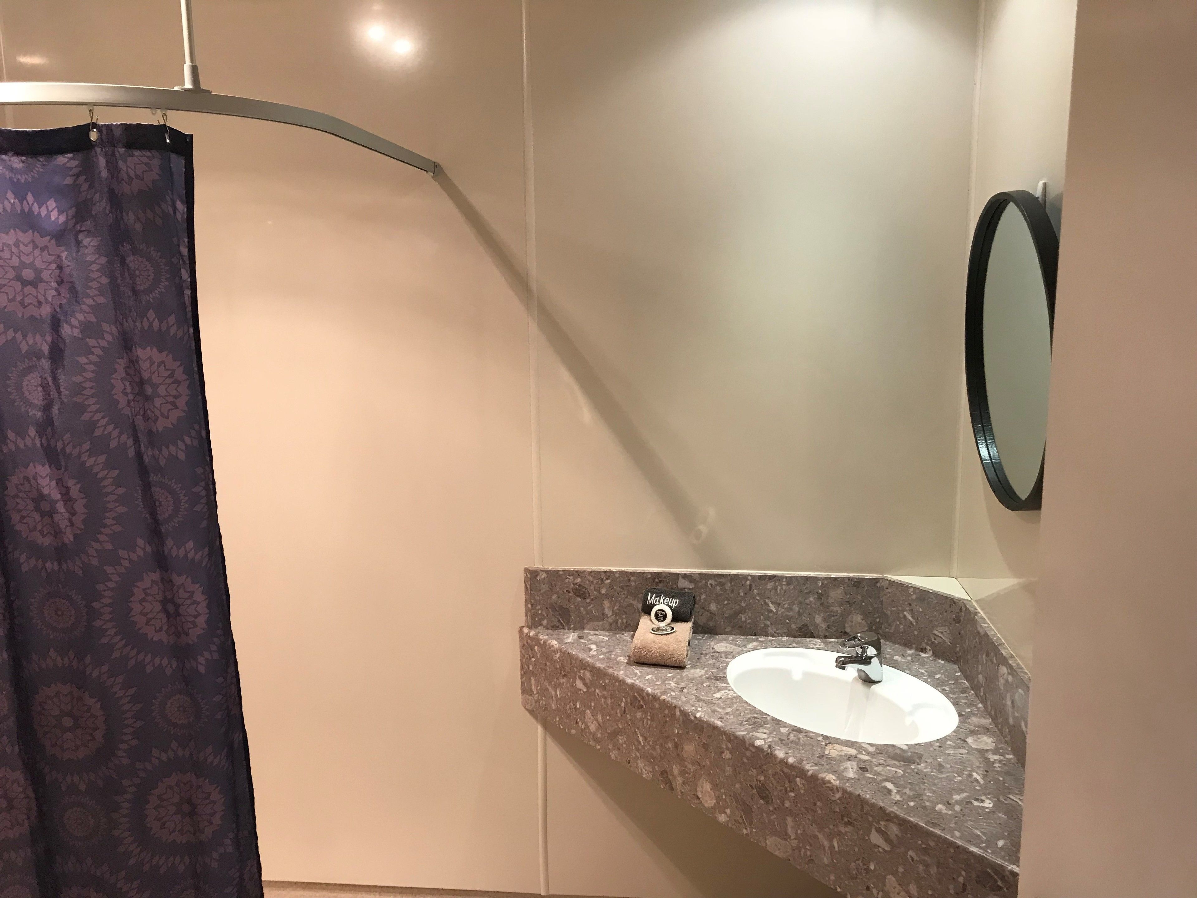 A bathroom with a curved shower curtain, a sink with a towel, and a mirror on the wall.