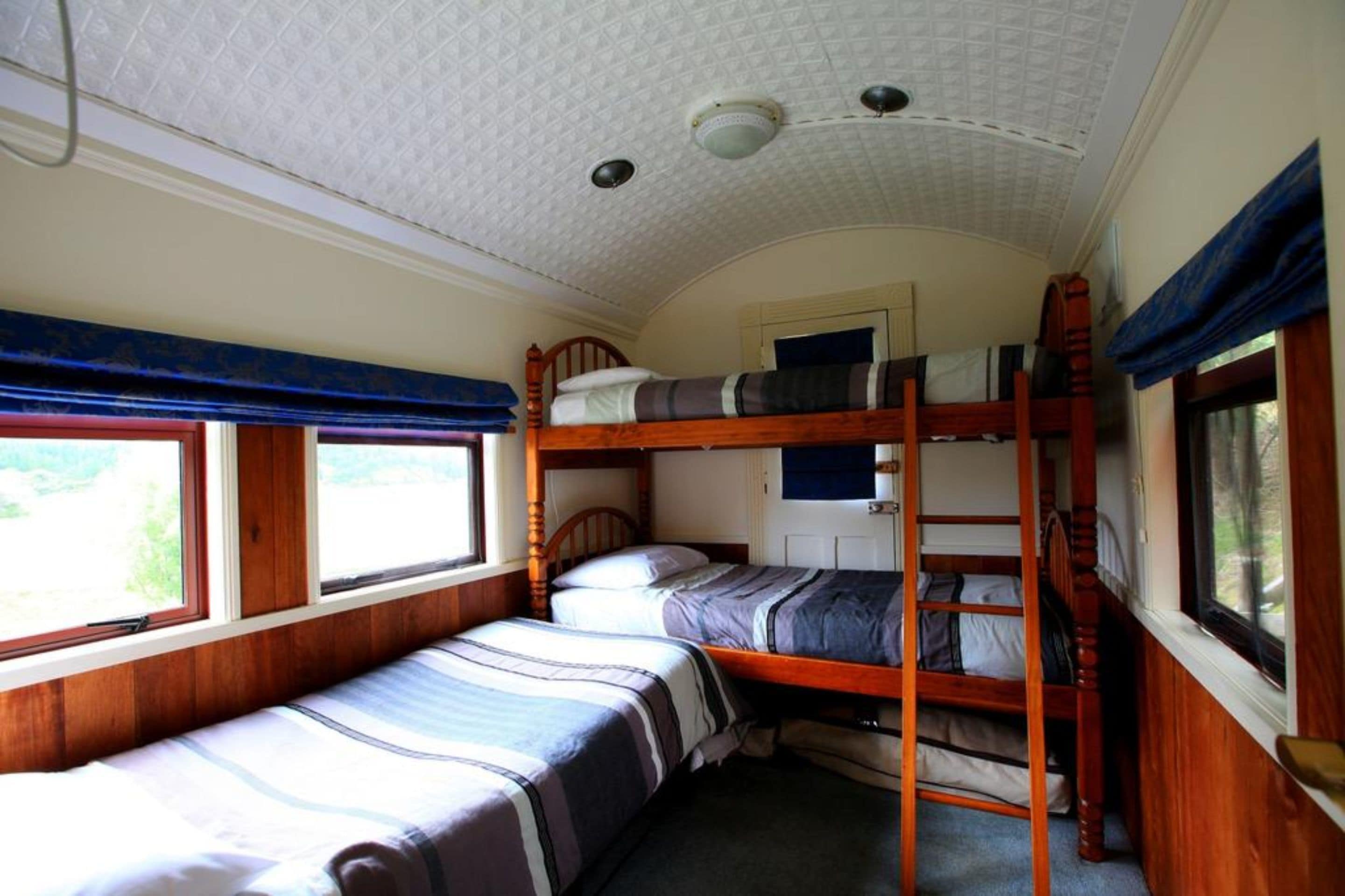 Een treincoupé met twee slaapplekken beneden en een slaapplek boven, houten wanden en een gestreept plafond.