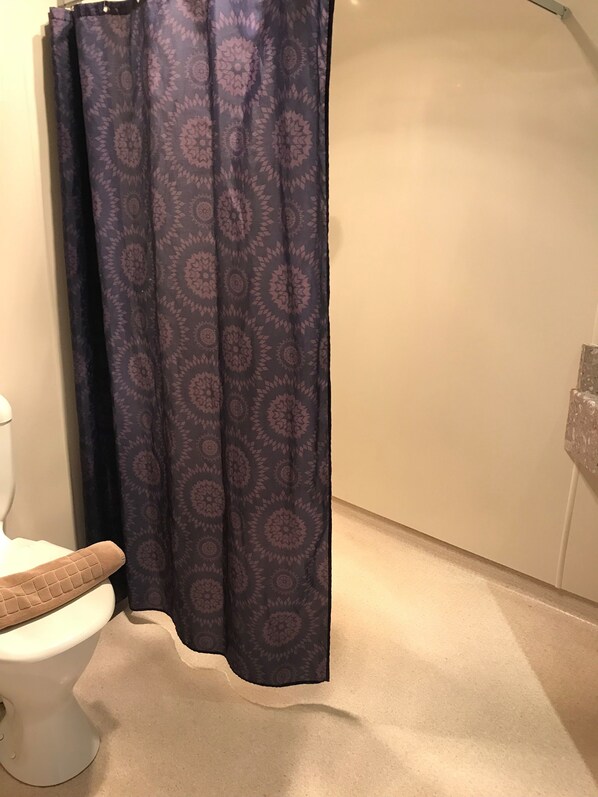 A bathroom with a toilet, a patterned shower curtain, and a beige floor. - Woodlyn Park (Waitomo Caves)
