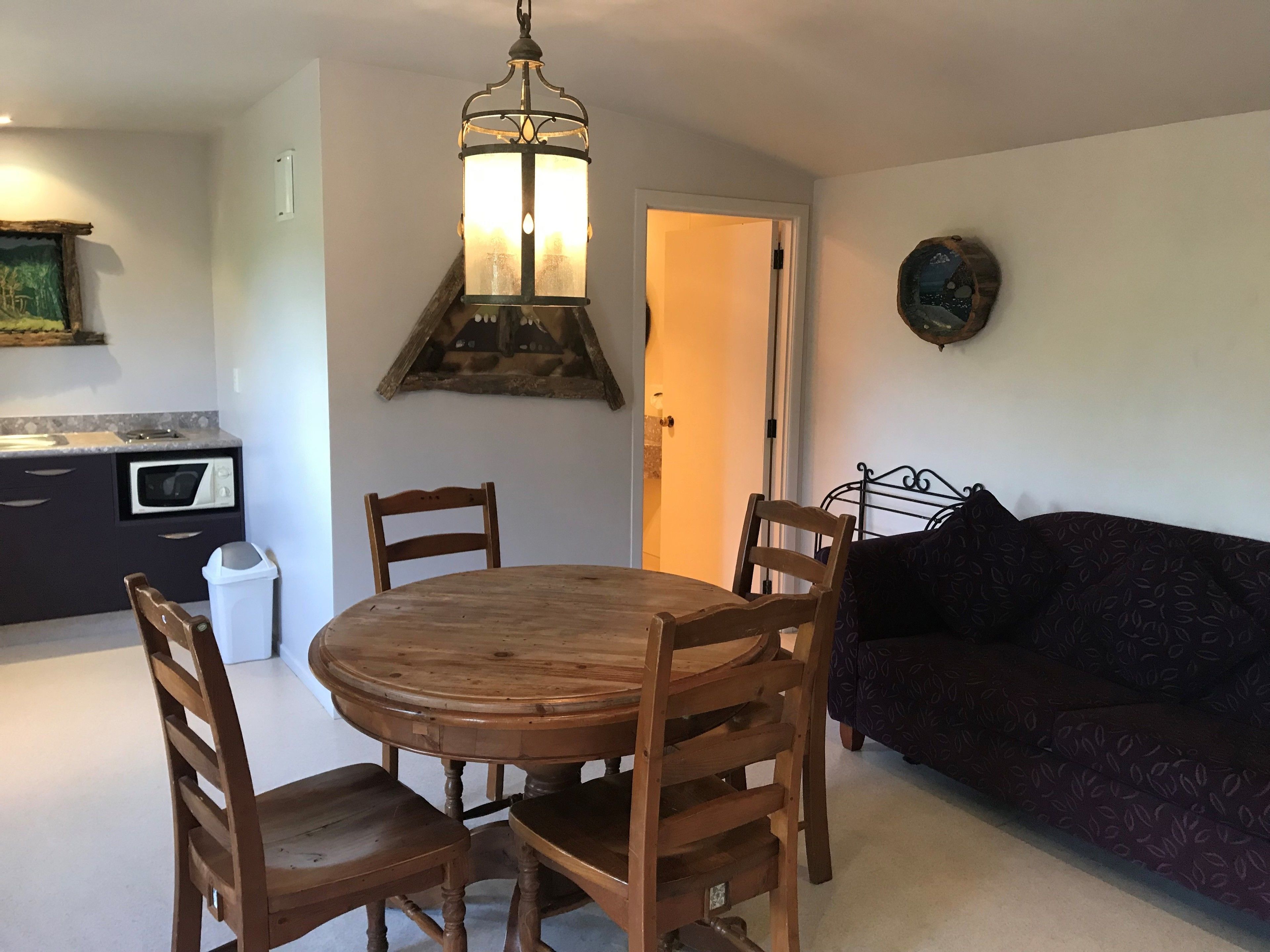 A dining area with a wooden table and chairs, a hanging light fixture, a microwave, and a sofa.