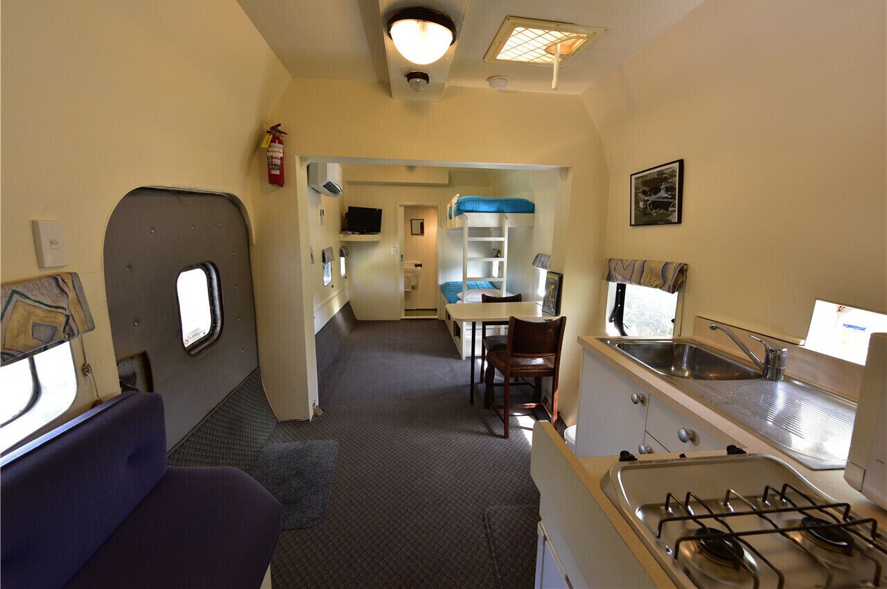 Una kitchenette compacta con estufa a gas, lavamanos y un pequeño comedor con mesa y sillas.