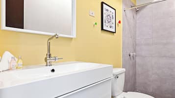 A bathroom with a white sink, a mirror, a toilet, and a shower area.