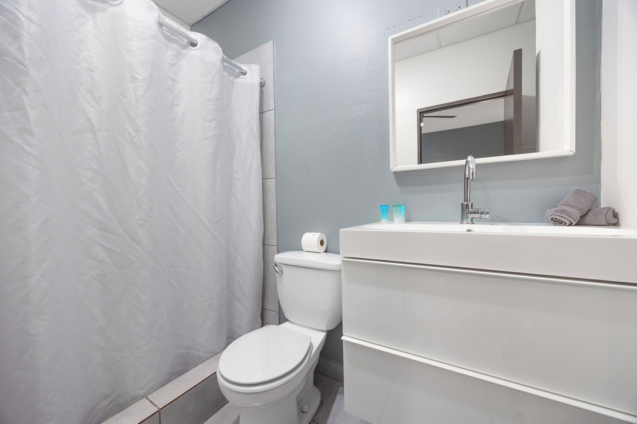 Een badkamer met toilet, douchegordijn, wastafel met spiegel en toiletartikelen.