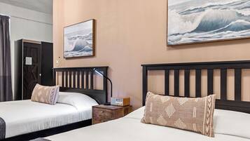 A hotel room with two beds, a nightstand with a radio, and two large ocean wave paintings on the walls.