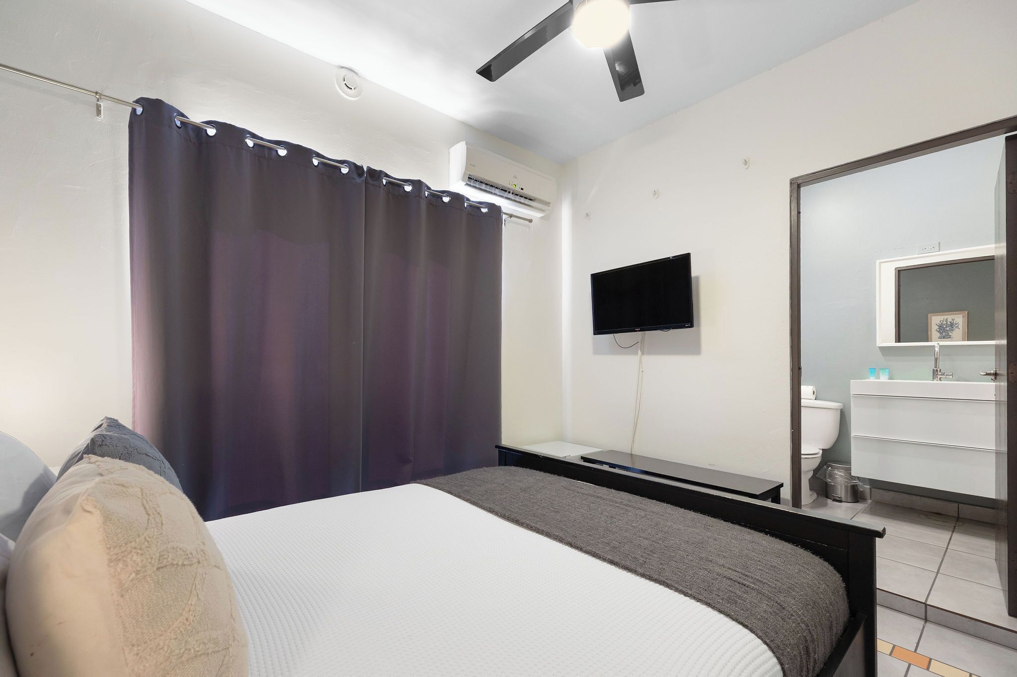Un dormitorio con cama, televisor de pantalla plana, espejo y aire acondicionado.