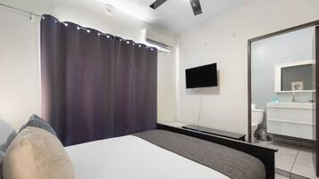 Un dormitorio con cama, televisor de pantalla plana, espejo y aire acondicionado.