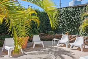 A patio area with white plastic chairs, a small table, and a large potted plant.