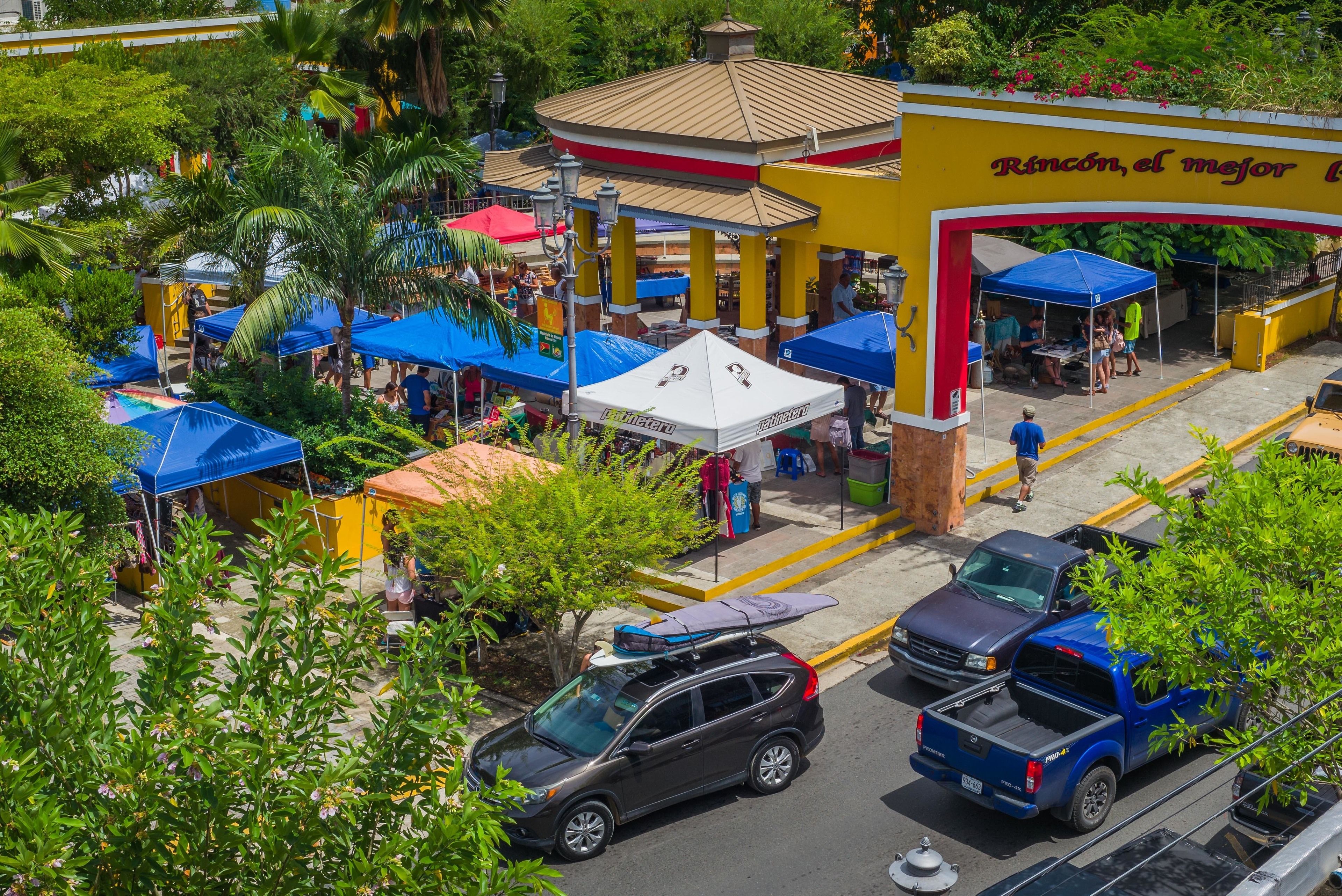 A street view with a yellow building labeled "Rincón, el mejor" and multiple blue tents.