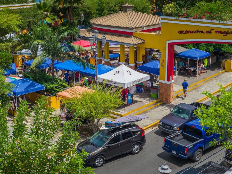 A street view with a yellow building labeled "Rincón, el mejor" and multiple blue tents.