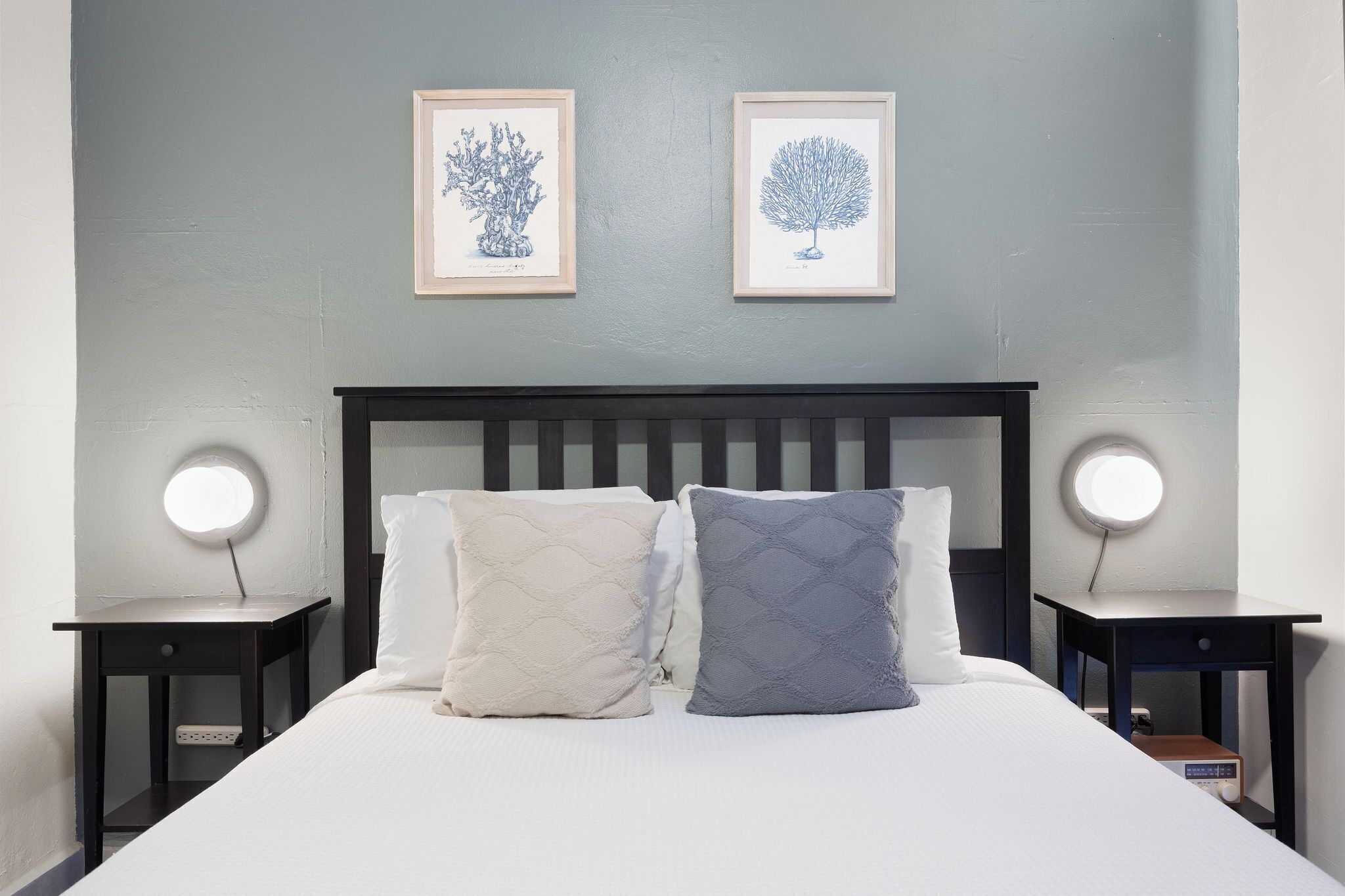 A neatly made bed with two pillows, a headboard, and bedside tables with round lights.