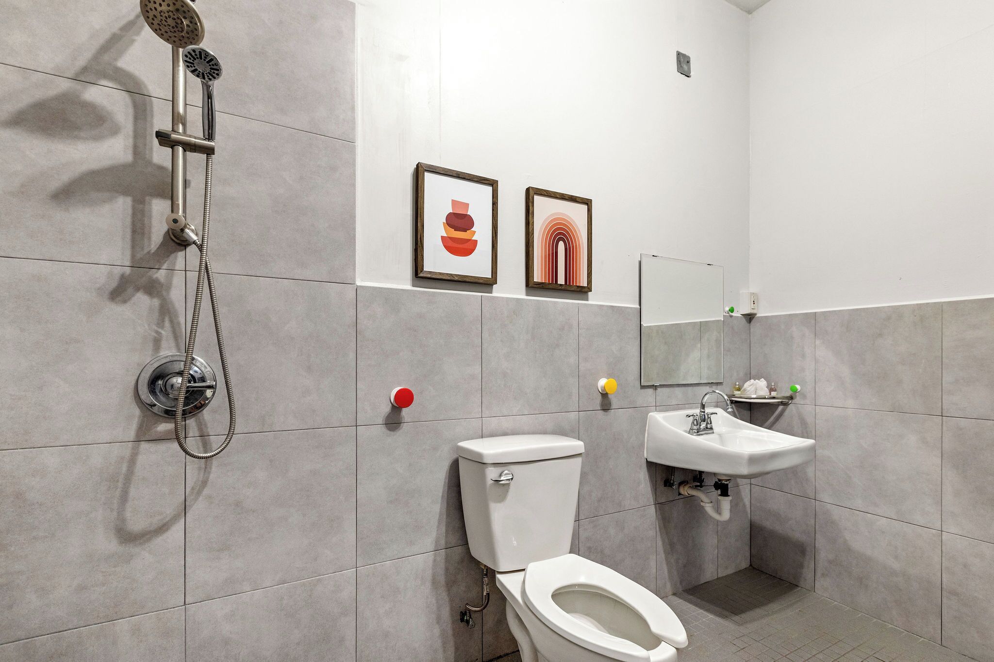 A modern bathroom with a shower, toilet, sink, and two framed artworks on the wall.