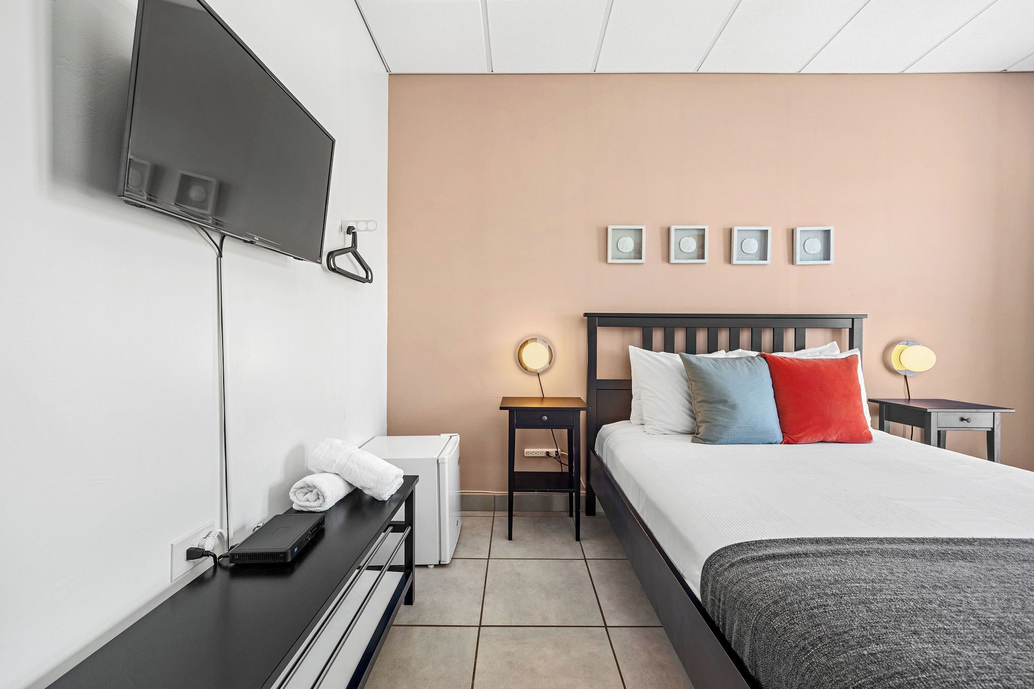 A hotel room with a bed, bedside tables, a TV mounted on the wall, and a wall-mounted light fixture.
