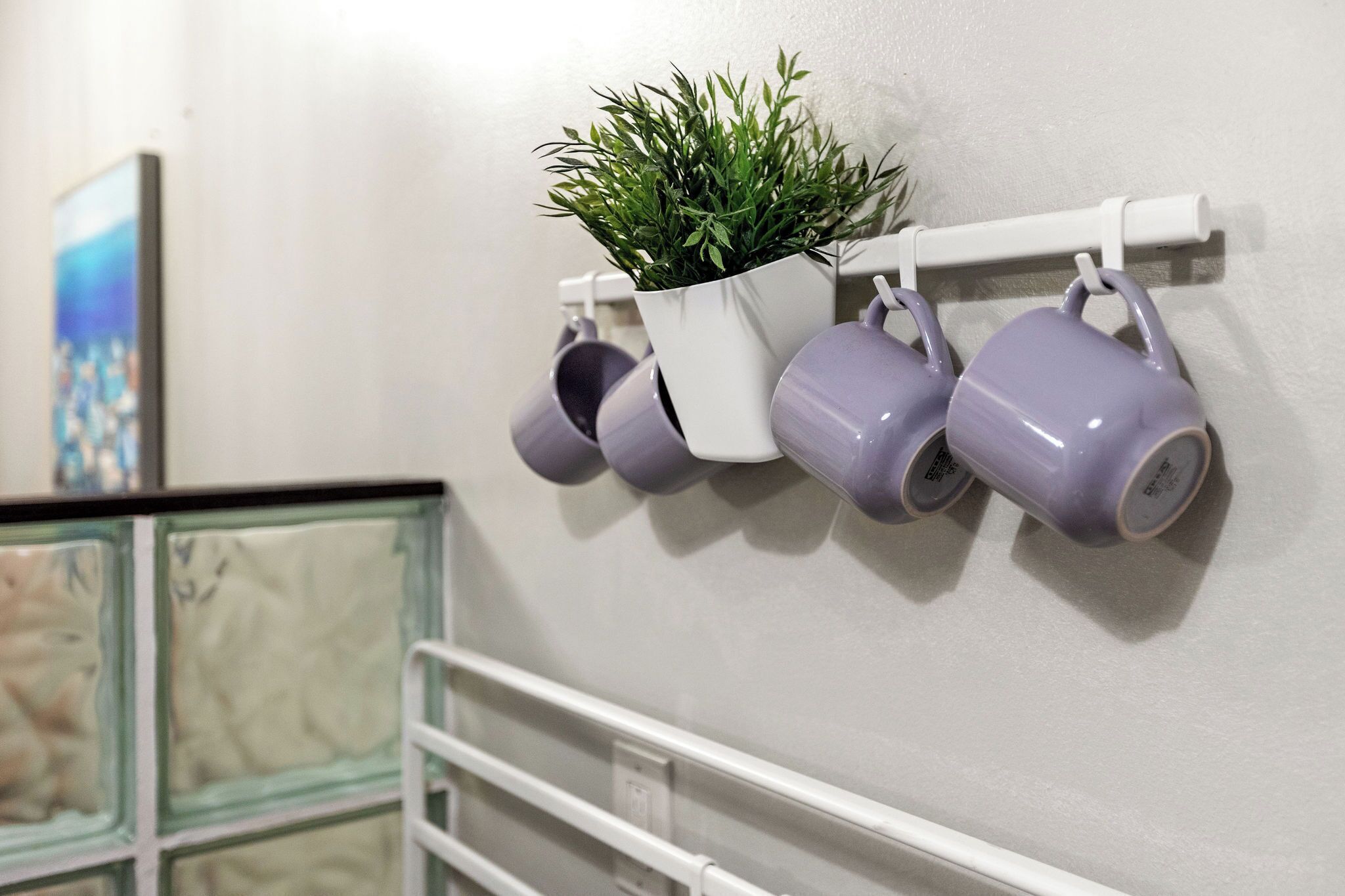 A wall-mounted shelf with a potted plant and several purple mugs.