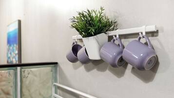 A wall-mounted shelf with a potted plant and several purple mugs.