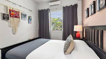Una habitación de hotel con cama, una mesita de noche con lámpara, ventana con cortinas y decoración en la pared.