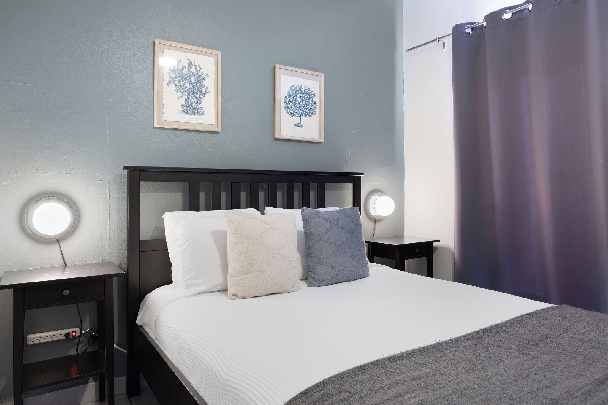 A neatly made bed with pillows, a bedside table with a lamp, and two framed pictures on the wall.