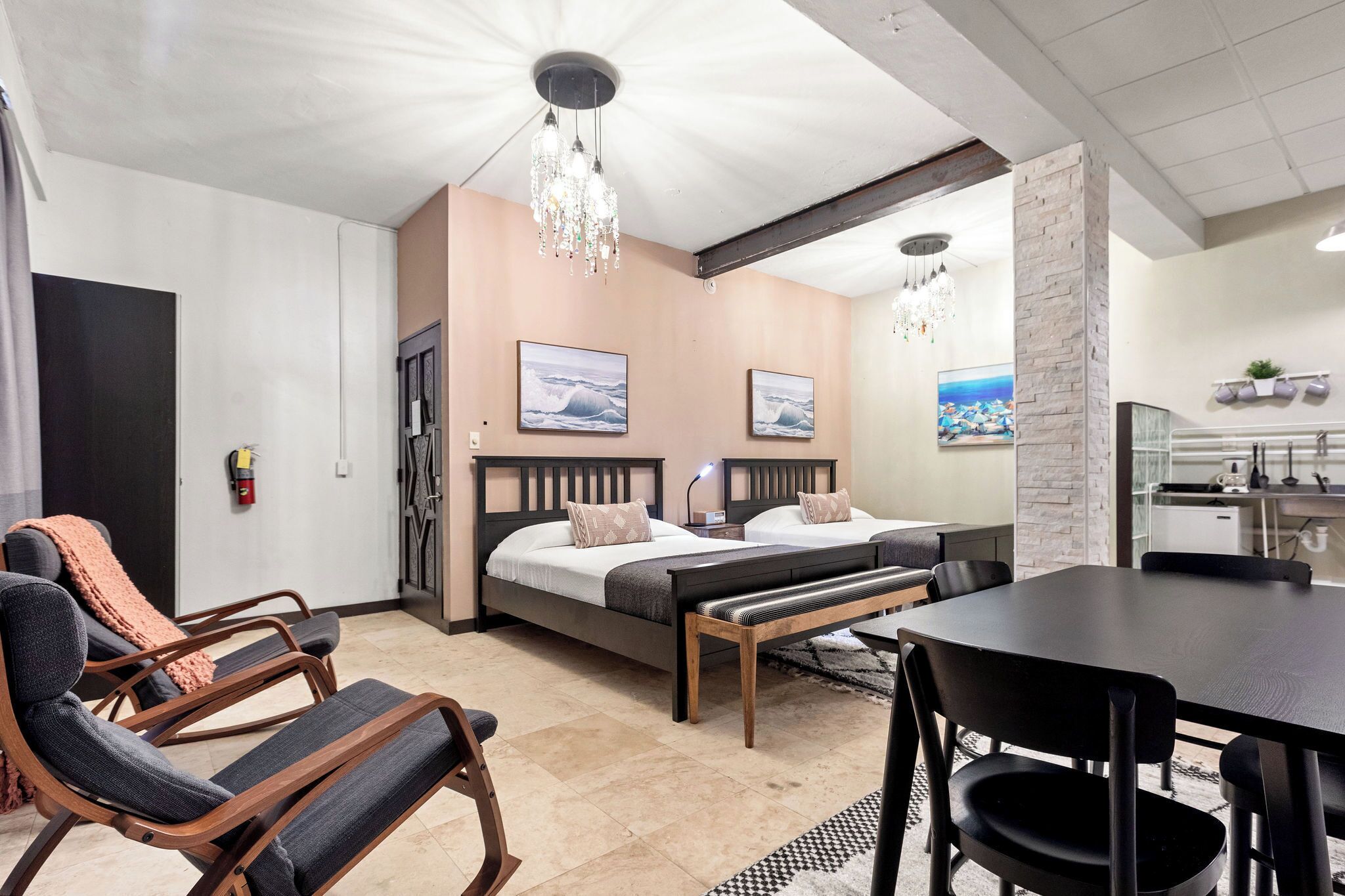 A hotel room with a bed, two bedside tables, a desk, a chair, a bench, a chandelier, and artwork on the walls.