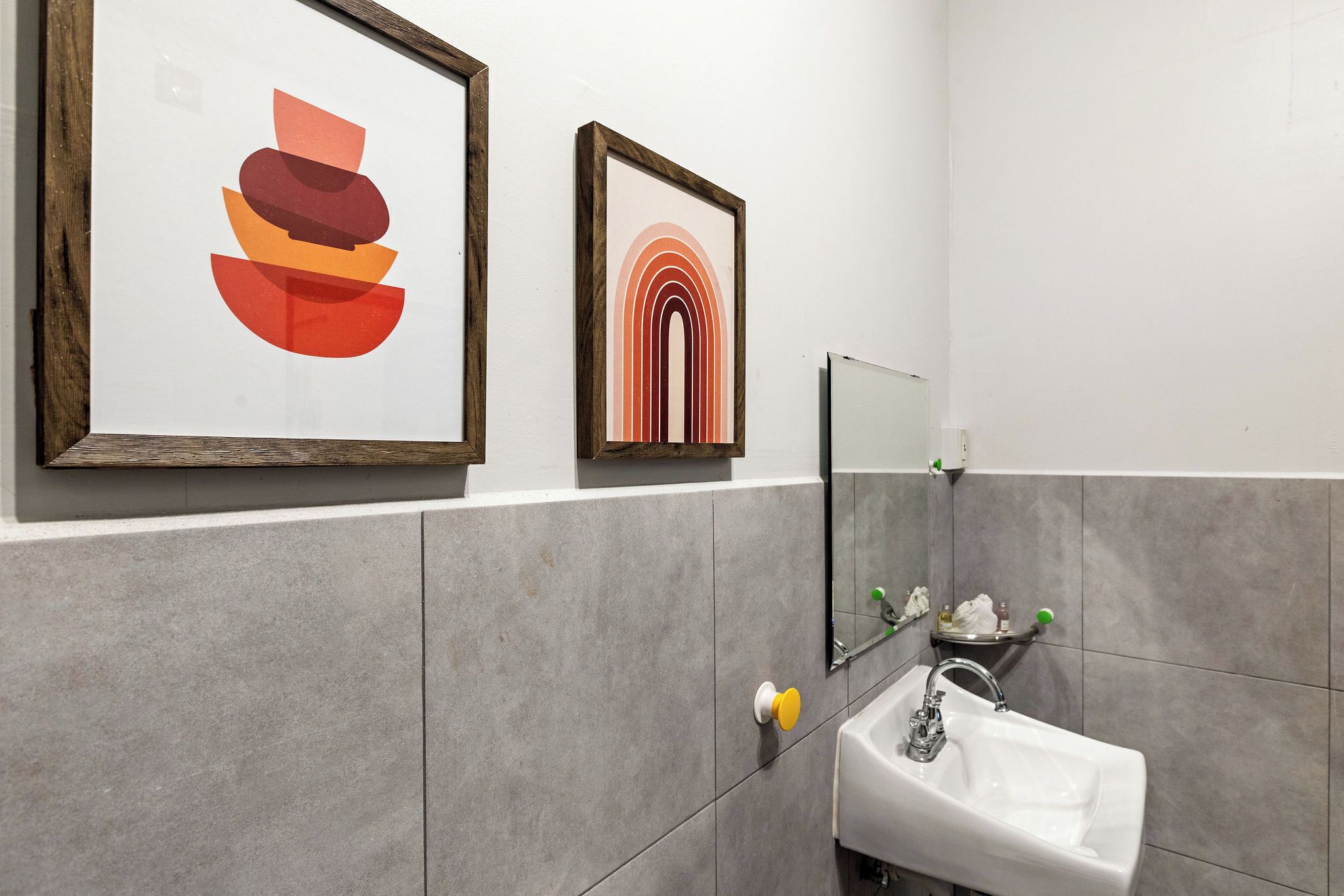 A bathroom with a white sink, a mirror, and two framed artworks on the wall.