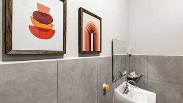 A bathroom with a white sink, a mirror, and two framed artworks on the wall.