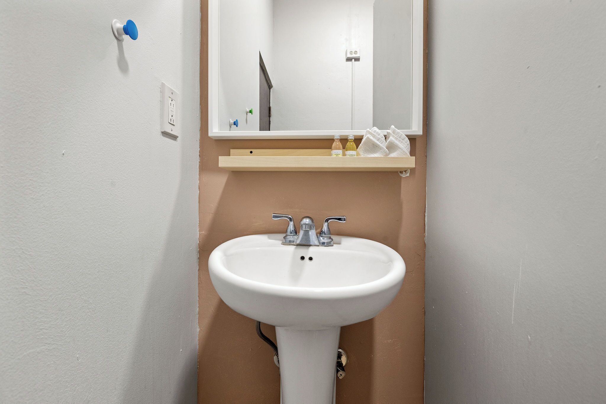 Een badkamer met een wit wastafelmeubel, een spiegel erboven en een plank met toiletartikelen.