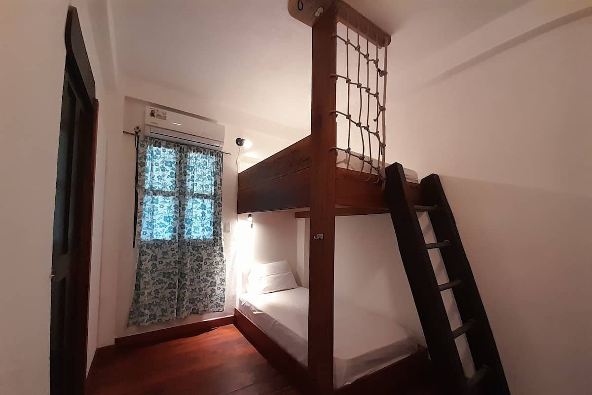 A small, compact room with a bunk bed, a window with floral curtains, and a wooden ladder.