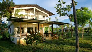 A two-story house with a covered porch, surrounded by lush greenery and a hammock. - Hotel Hibiscus Garden / Jardin De Papos (Hicaco)