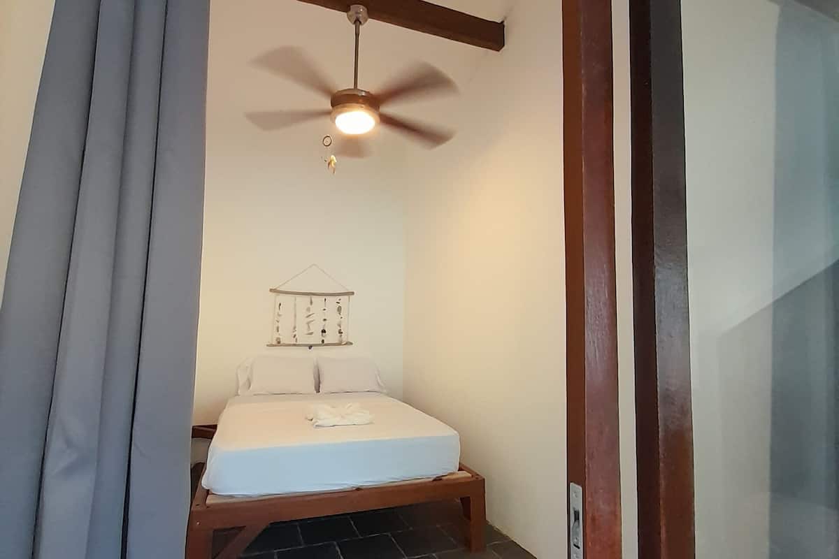 A bedroom with a bed, a ceiling fan, and a stone-tiled floor.