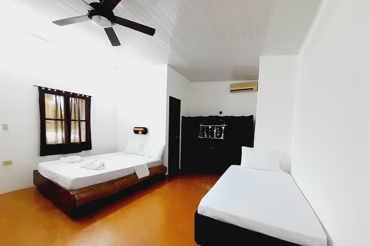 A room with two beds, a ceiling fan, a window with curtains, and a wall-mounted heater.