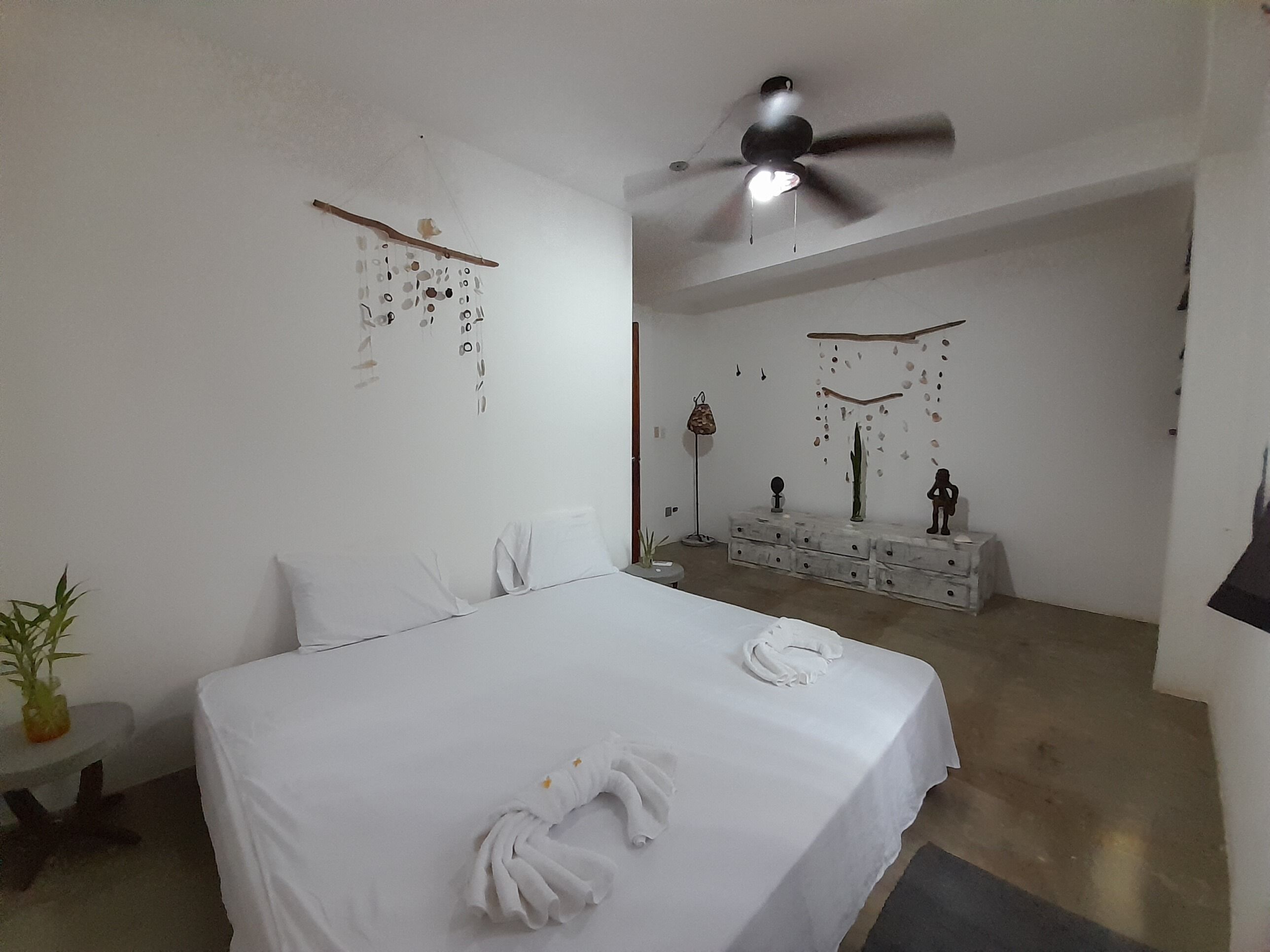 Une chambre à coucher comprenant un lit, un ventilateur de plafond, une commode et des éléments de décoration murale.