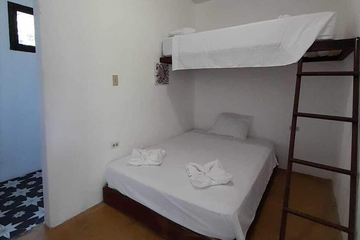 A small, single-bed room with a bunk bed above, a wooden ladder, and a small window.