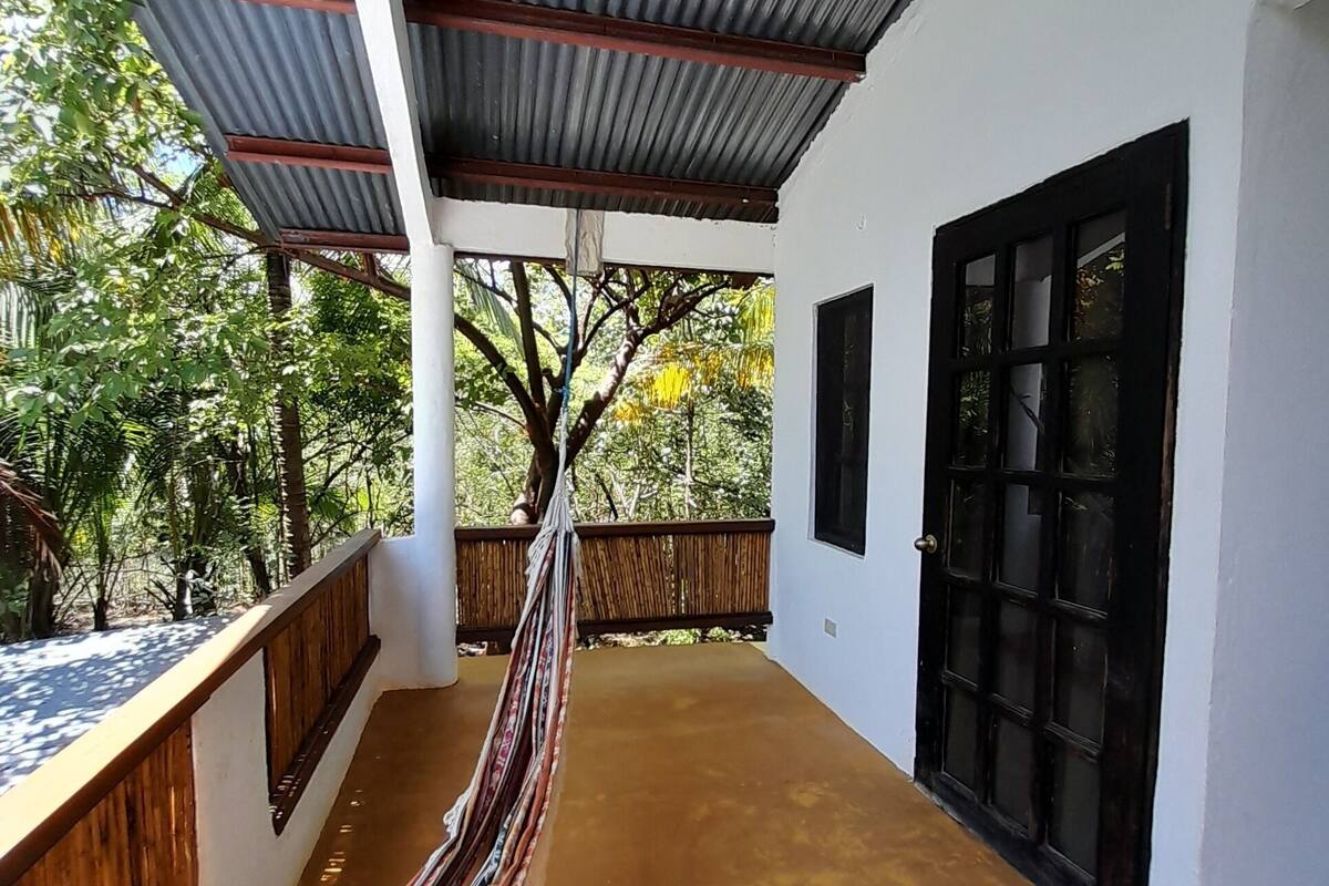 A covered outdoor area with a hammock, a wooden bench, and a black door.