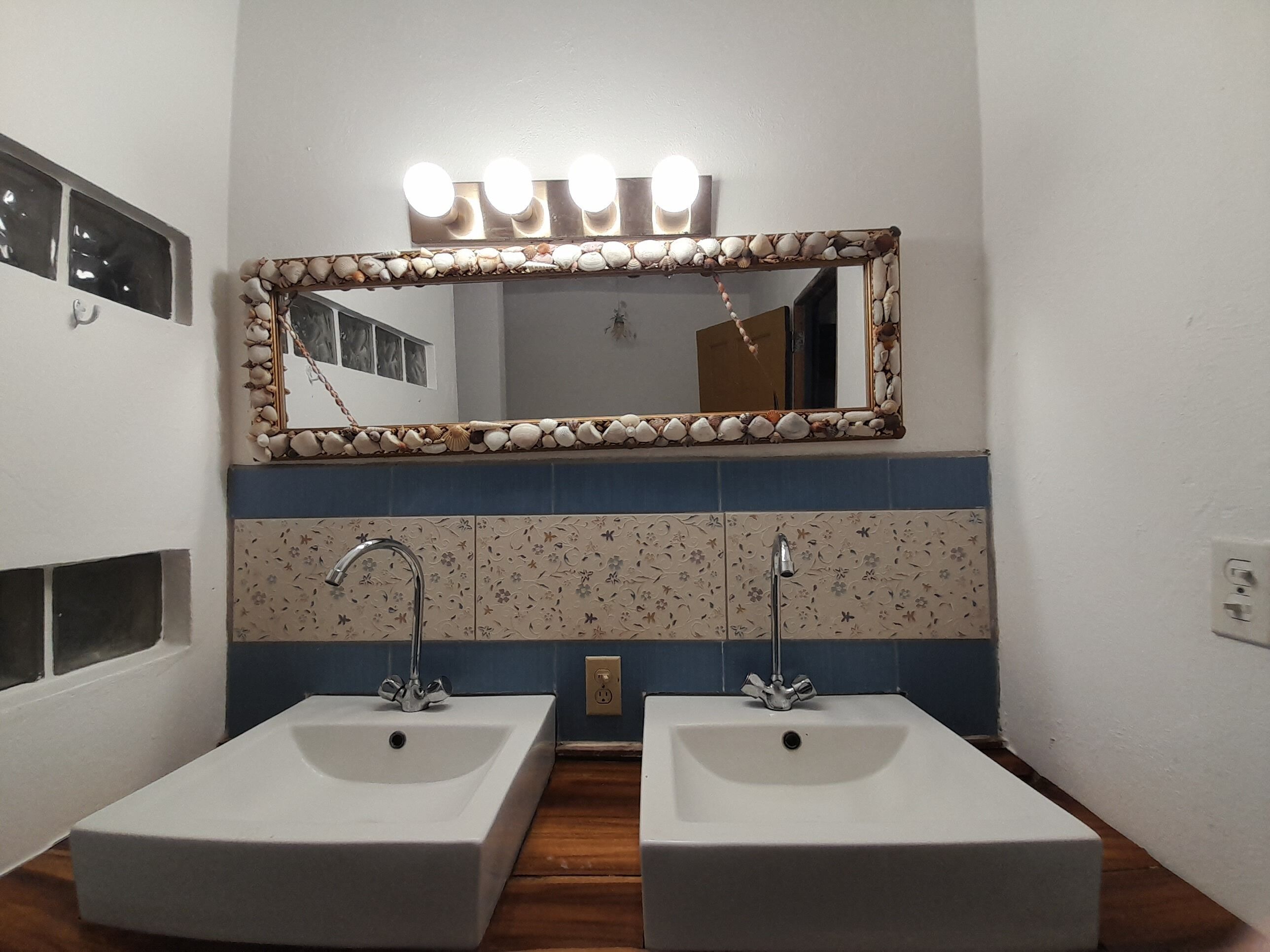 Casa de banho com duas pias, um espelho com luzes e azulejos estampados.