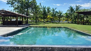 A rectangular swimming pool with clear water, surrounded by a grassy area and trees. - Hotel Hibiscus Garden / Jardin De Papos (Hicaco)