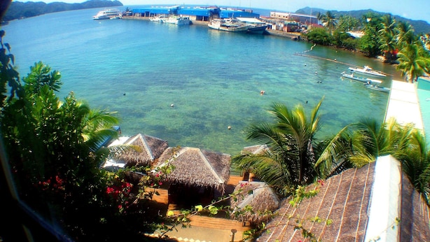 Un resort tropical con cabañas de techo de paja, una piscina y aguas azules cristalinas con barcos.