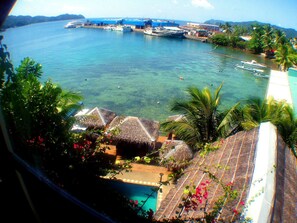A tropical resort with thatched-roof huts, a swimming pool, and clear blue waters with boats.